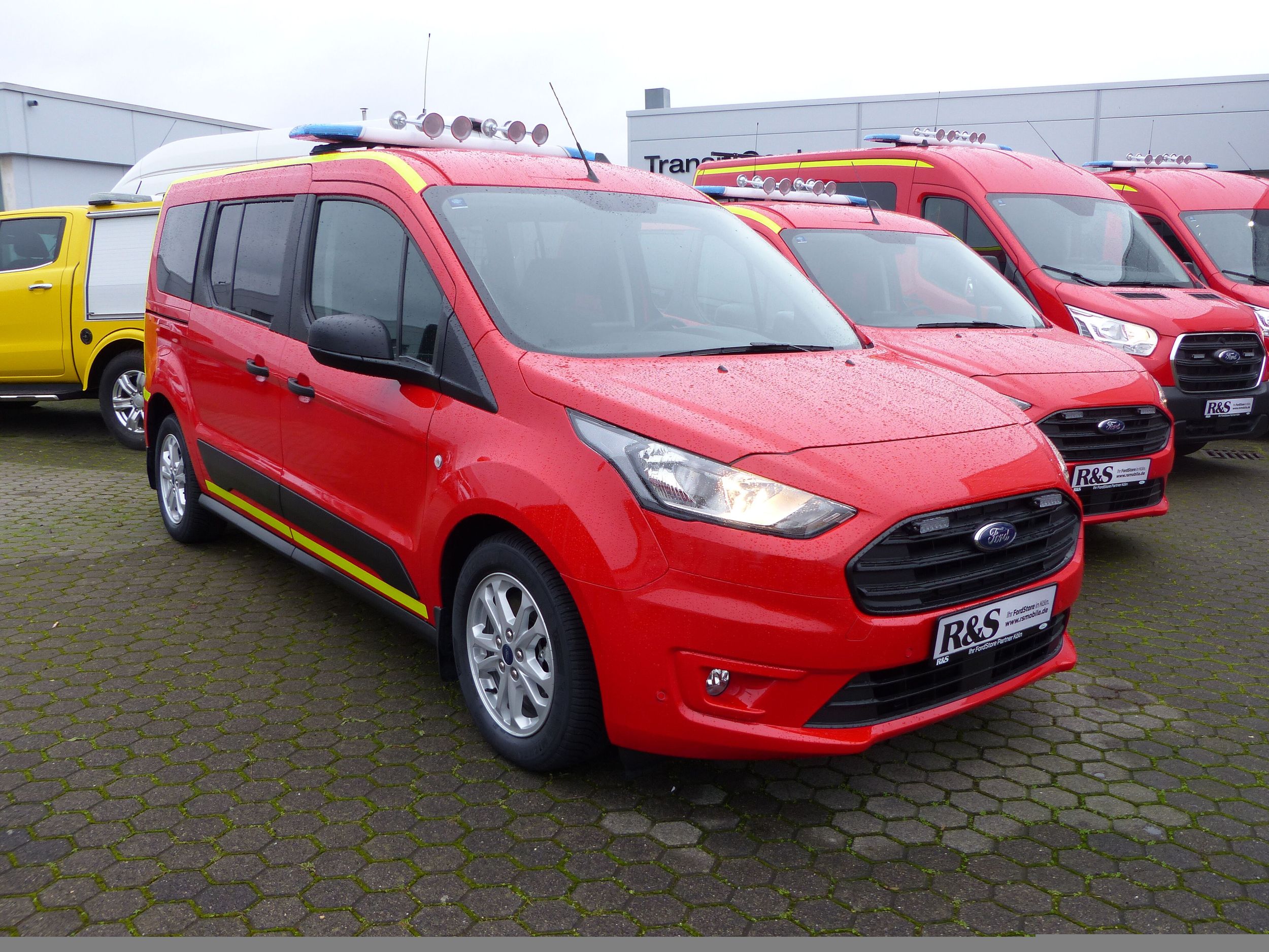 Ein roter Transporter mit gelben Warnstreifen seitlich von vorne gezeigt