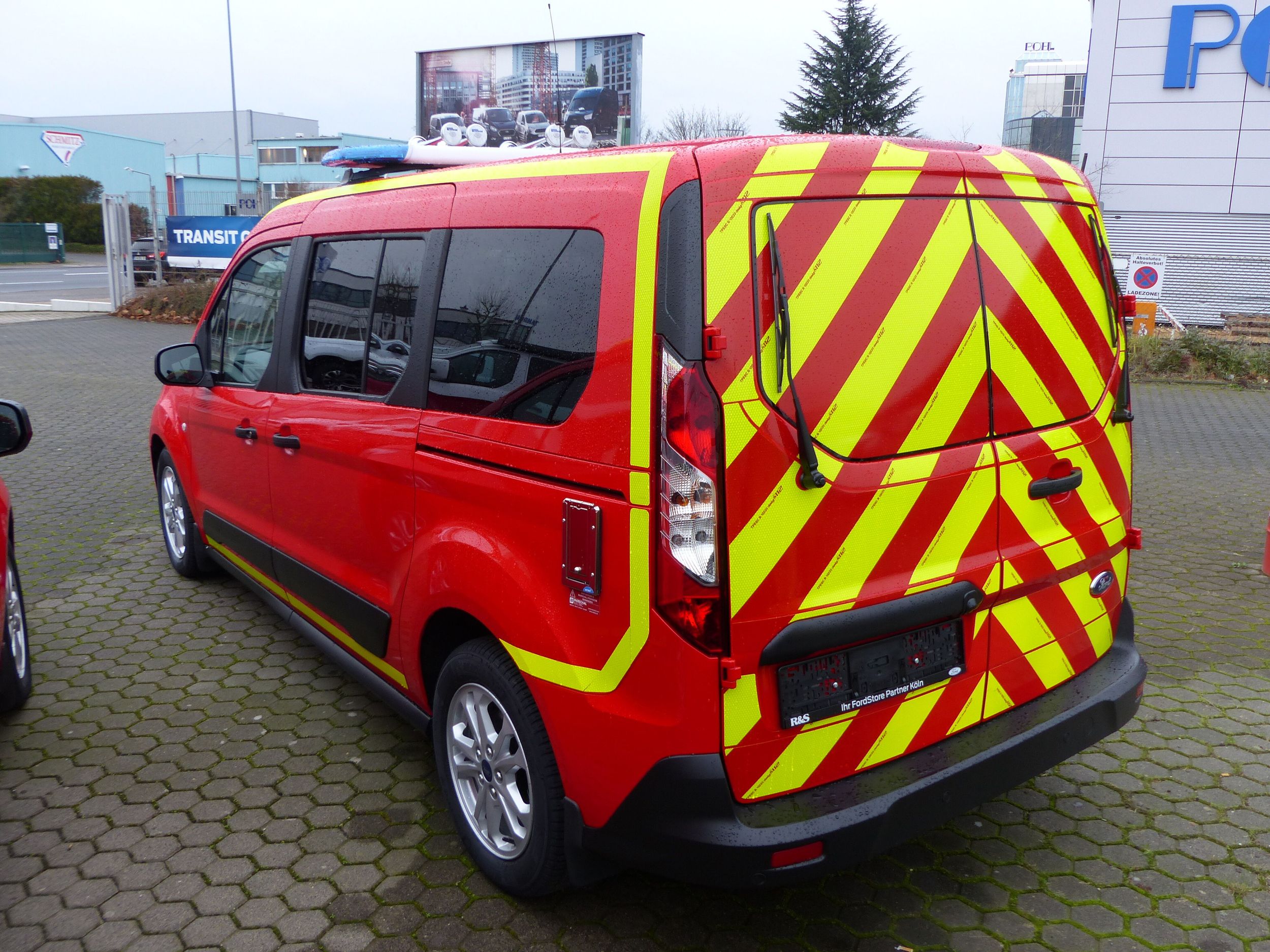 Ein roter Transporter mit gelben Warnstreifen seitlich von hinten gezeigt