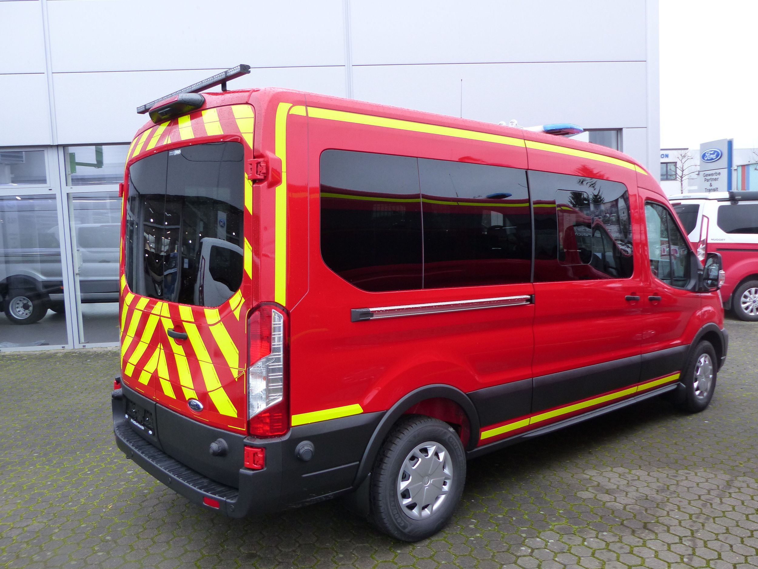 Ein roter Transporter mit gelben Warnstreifen seitlich von hinten gezeigt
