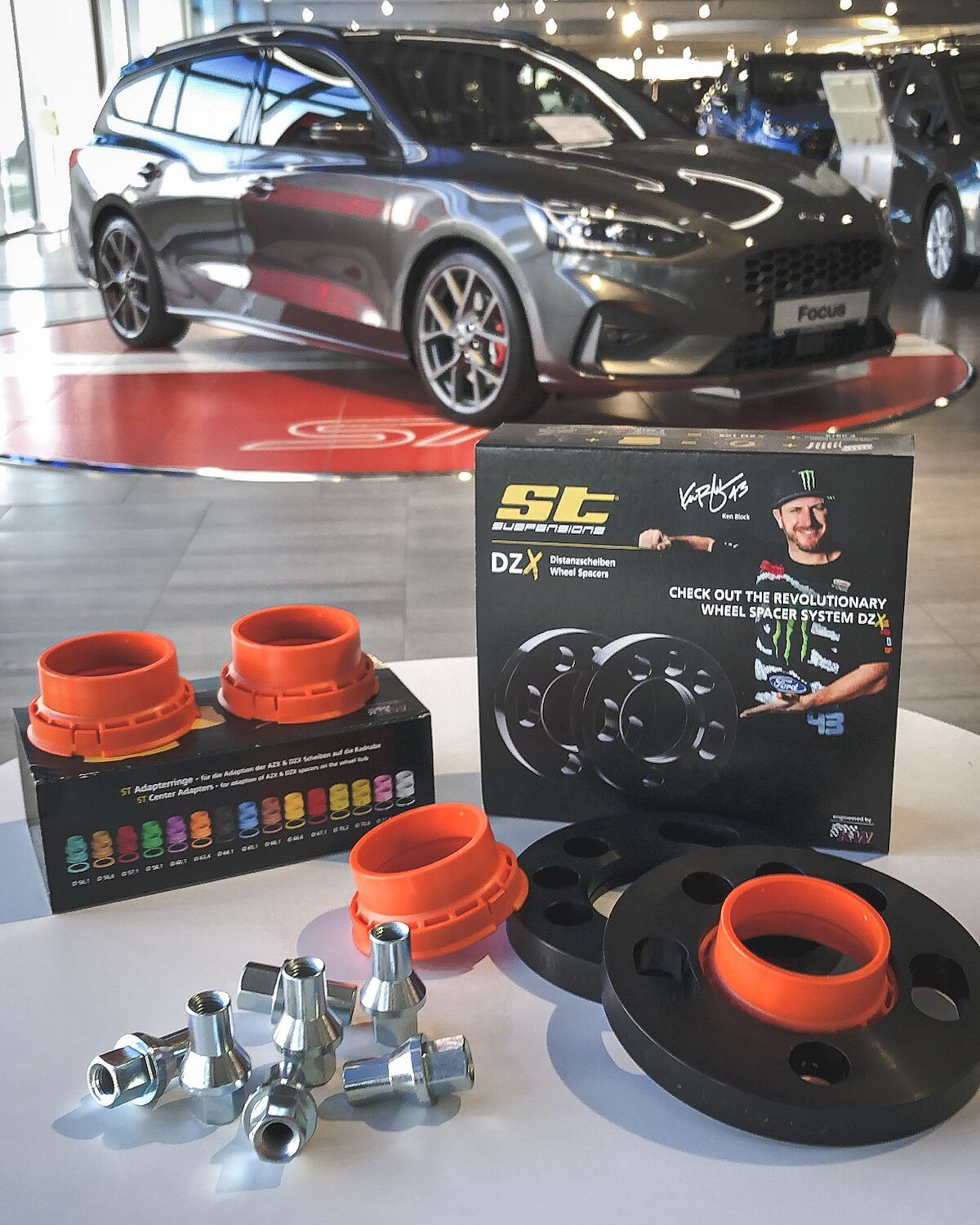 Zu sehen ist im Vordergrund das ausgepackte Suspension-Kit; im Hintergrund ist ein neuer Ford Focus im Autohaus zu sehen